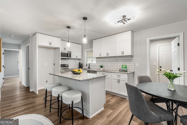 kitchen featuring stainless steel appliances, a breakfast bar, dark wood-style flooring, a kitchen island, and white cabinets