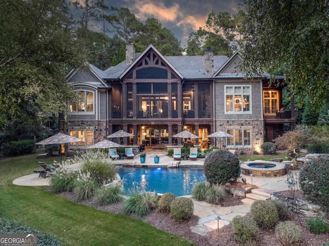 rear view of property with a fire pit, an outdoor pool, a patio, stone siding, and a chimney