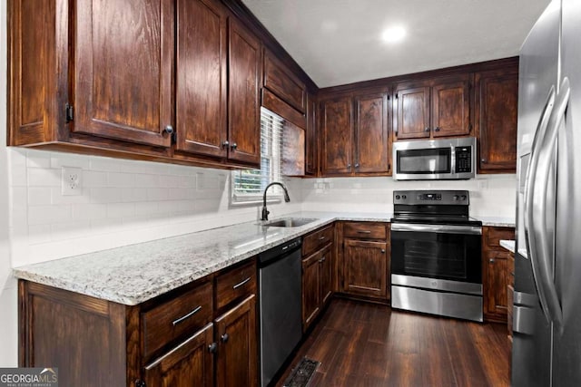 kitchen with dark wood-style flooring, appliances with stainless steel finishes, light stone counters, and a sink