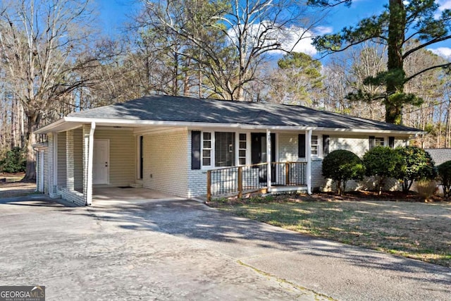 ranch-style home with an attached carport, covered porch, brick siding, and driveway