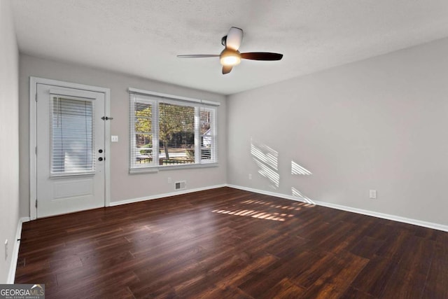 unfurnished room featuring dark wood-style flooring, visible vents, ceiling fan, and baseboards