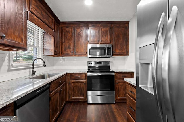 kitchen with tasteful backsplash, dark wood finished floors, appliances with stainless steel finishes, light stone counters, and a sink