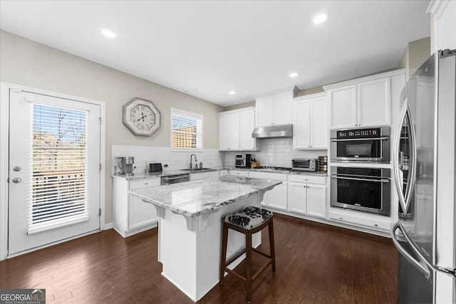 kitchen with dark wood-type flooring, under cabinet range hood, a sink, backsplash, and stainless steel appliances