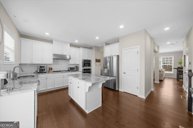 kitchen with a sink, under cabinet range hood, dark wood-style floors, appliances with stainless steel finishes, and light stone countertops
