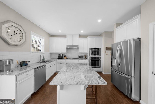 kitchen with a sink, stainless steel appliances, under cabinet range hood, backsplash, and a center island