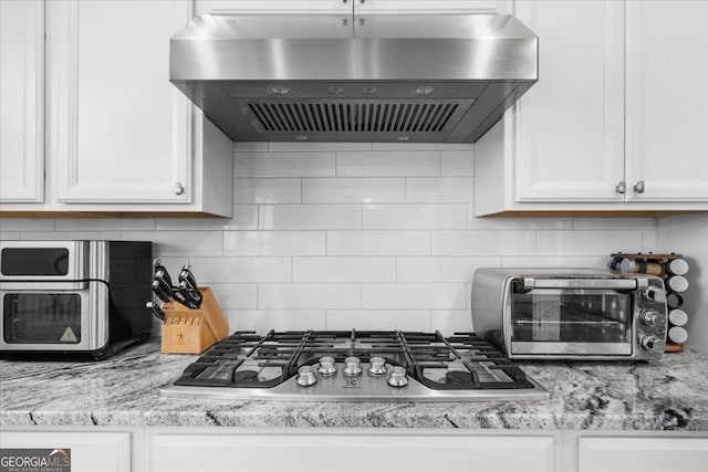 kitchen with backsplash, range hood, white cabinetry, a toaster, and stainless steel gas cooktop