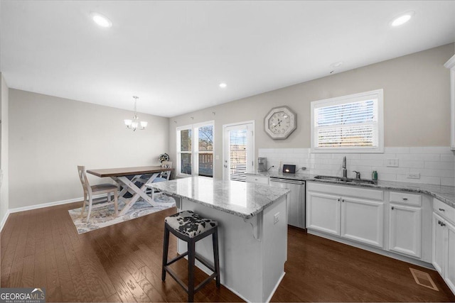 kitchen featuring a sink, dark wood-type flooring, light stone counters, an inviting chandelier, and stainless steel dishwasher