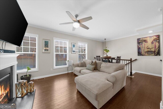 living room with baseboards, dark wood-type flooring, a warm lit fireplace, and a ceiling fan