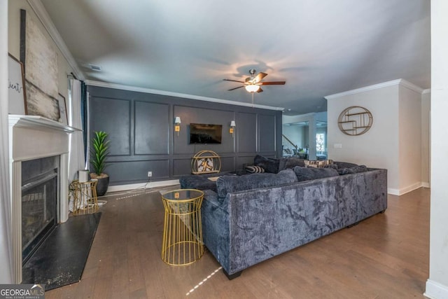 living area featuring a fireplace with raised hearth, crown molding, dark wood finished floors, and a decorative wall