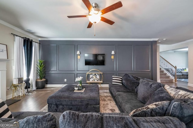 living room featuring dark wood finished floors, ceiling fan, stairway, ornamental molding, and a decorative wall