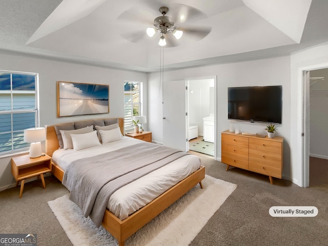 bedroom with a tray ceiling, dark carpet, a ceiling fan, connected bathroom, and baseboards