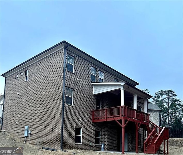 rear view of house featuring stairway, brick siding, and a wooden deck