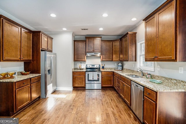 kitchen featuring hardwood / wood-style flooring, under cabinet range hood, stainless steel appliances, a sink, and crown molding