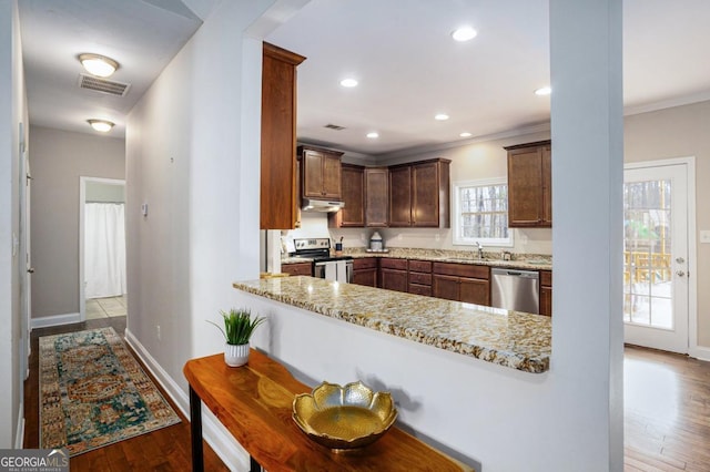 kitchen with appliances with stainless steel finishes, crown molding, under cabinet range hood, and wood finished floors