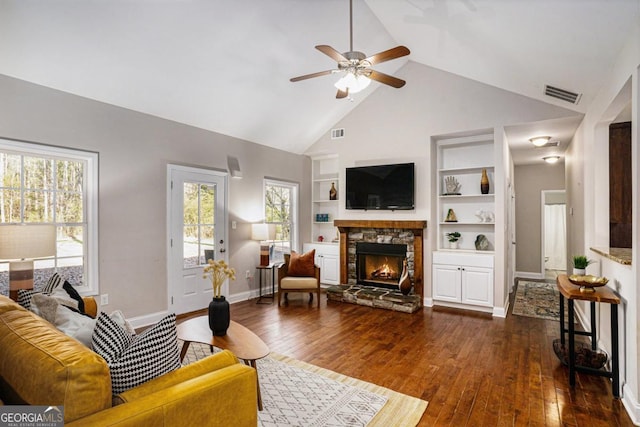 living room featuring hardwood / wood-style flooring, built in shelves, visible vents, and a stone fireplace