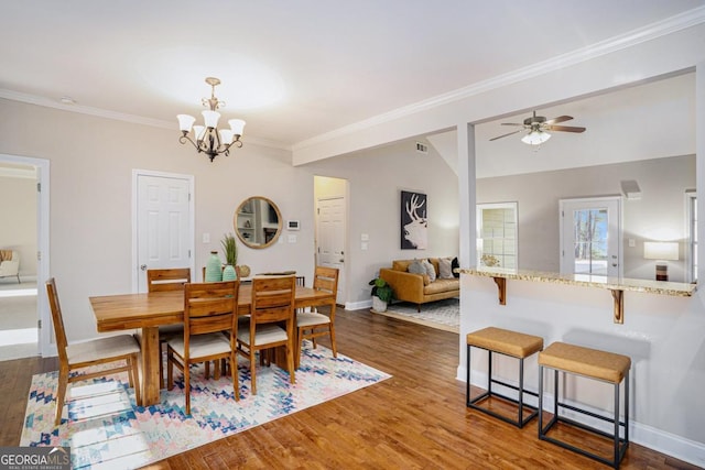 dining space featuring dark wood finished floors, ornamental molding, vaulted ceiling, baseboards, and ceiling fan with notable chandelier