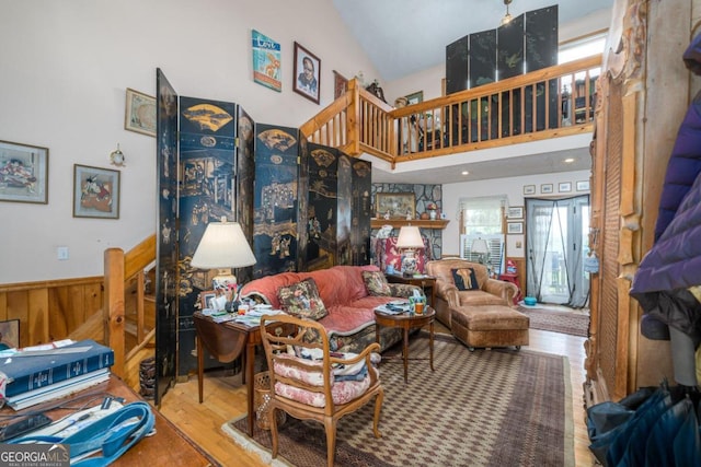 living area with wainscoting, stairway, wood finished floors, wood walls, and high vaulted ceiling