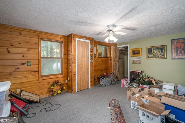 miscellaneous room with a textured ceiling, carpet floors, ceiling fan, and wooden walls