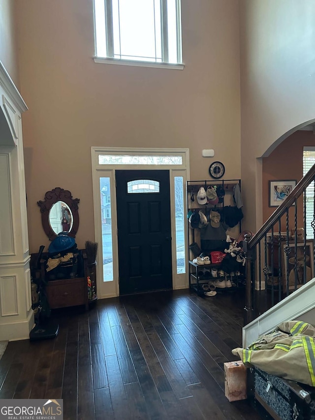 foyer featuring stairs, a high ceiling, arched walkways, and dark wood-type flooring