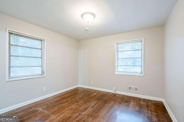 spare room with dark wood-style flooring, visible vents, and baseboards