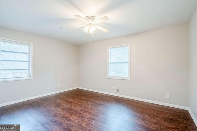 unfurnished room with plenty of natural light, visible vents, baseboards, and dark wood finished floors