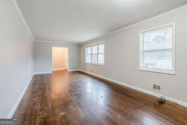 empty room with dark wood-style flooring, visible vents, crown molding, and baseboards