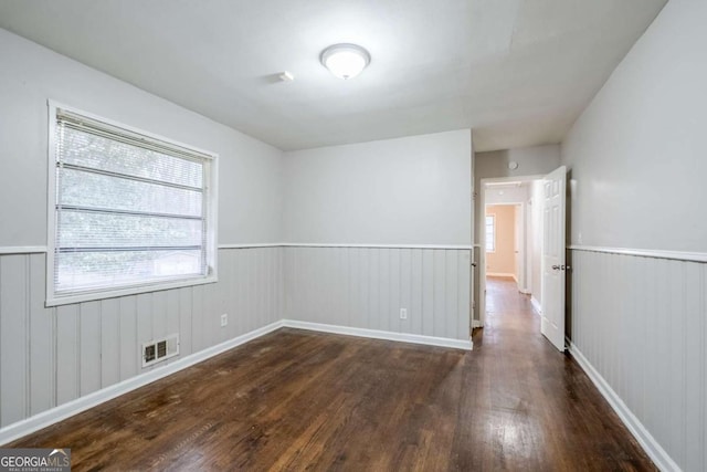 empty room with dark wood-style flooring, wainscoting, and visible vents