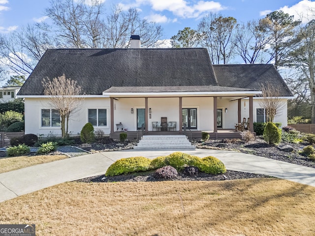 view of front of home with a porch, roof with shingles, a chimney, and stucco siding