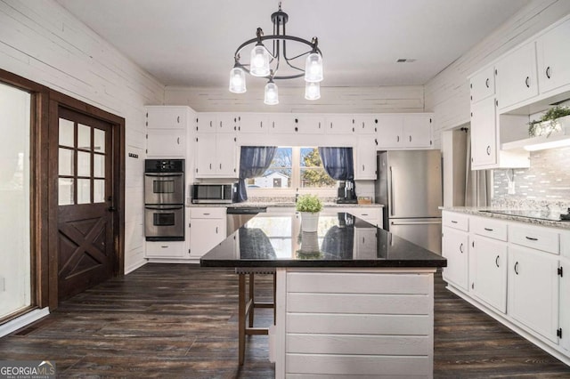 kitchen with white cabinets, appliances with stainless steel finishes, dark stone countertops, decorative light fixtures, and a center island