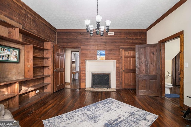 unfurnished living room featuring dark wood-style floors, wooden walls, a fireplace with raised hearth, and a textured ceiling