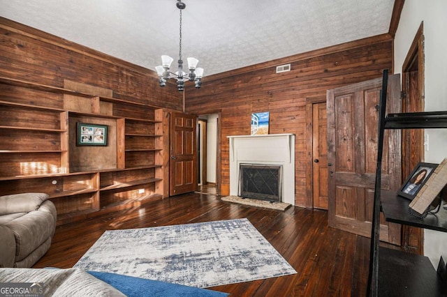 living room featuring a notable chandelier, visible vents, a fireplace with raised hearth, dark wood-type flooring, and wooden walls