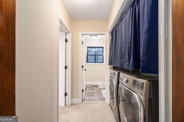 clothes washing area featuring washing machine and clothes dryer, light colored carpet, a textured ceiling, laundry area, and baseboards