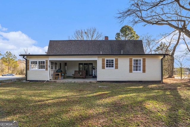 rear view of property featuring a yard, a shingled roof, a patio, and a chimney