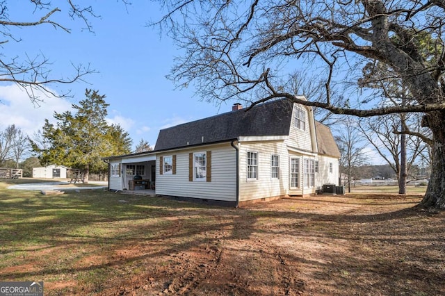 view of home's exterior with a gambrel roof, a yard, roof with shingles, crawl space, and a chimney