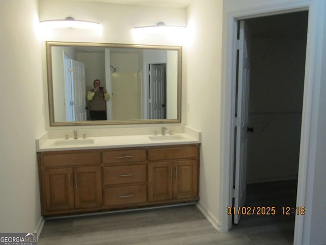 full bath with wood finished floors, a sink, baseboards, and double vanity