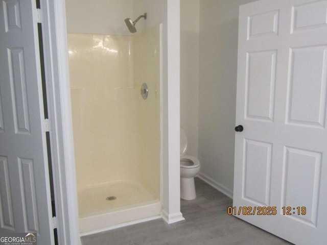 full bath featuring a shower stall, toilet, and wood finished floors