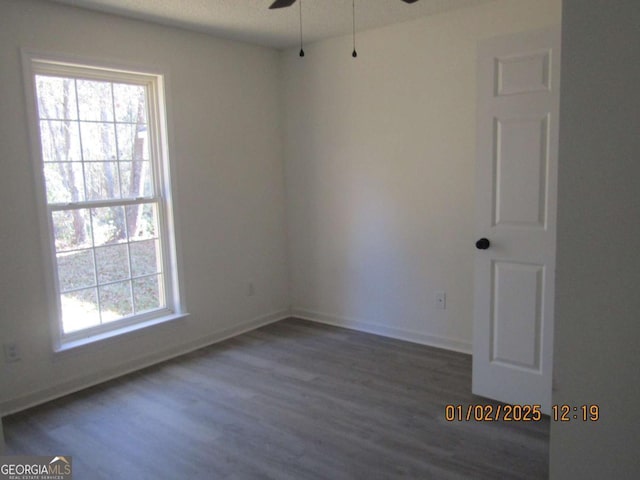 empty room featuring a ceiling fan, a healthy amount of sunlight, dark wood finished floors, and baseboards