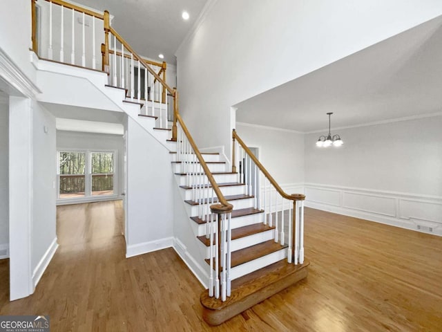 stairs featuring a chandelier, crown molding, a towering ceiling, and wood finished floors