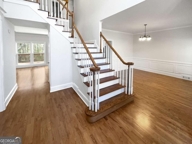 stairway with wood finished floors, visible vents, wainscoting, an inviting chandelier, and crown molding