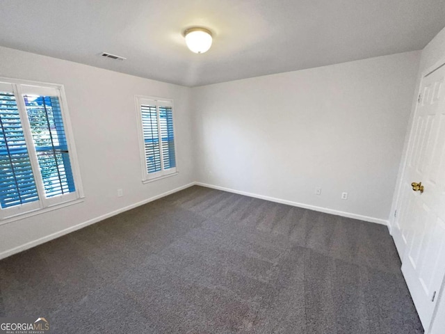 empty room with dark carpet, visible vents, and baseboards