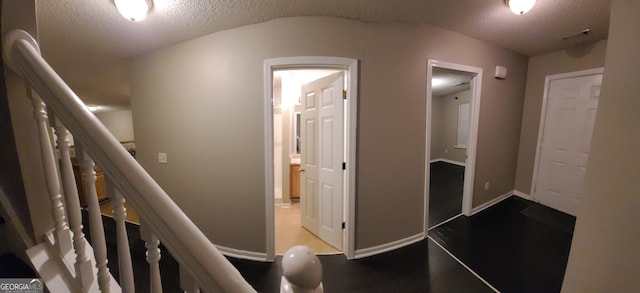 hall with a textured ceiling, stairs, light wood-style flooring, and baseboards