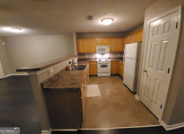 kitchen featuring light brown cabinets, a peninsula, white appliances, a sink, and dark countertops