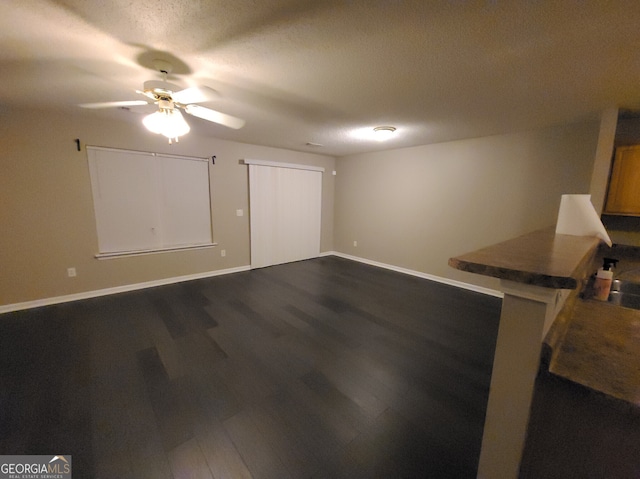 interior space featuring dark wood-style floors, a textured ceiling, a ceiling fan, and baseboards