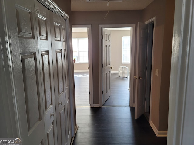 hall featuring dark wood-style floors, attic access, and baseboards