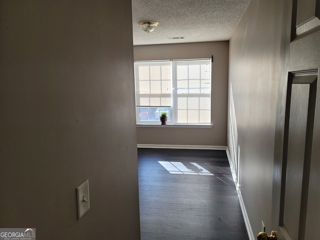 empty room with dark wood finished floors, a textured ceiling, and baseboards