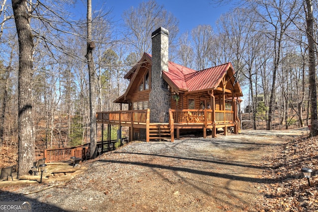 view of side of home featuring a deck, metal roof, dirt driveway, log exterior, and a chimney