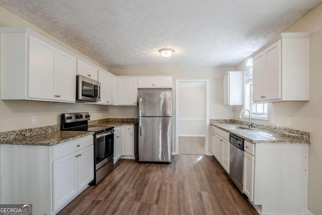 kitchen with appliances with stainless steel finishes, dark wood-style flooring, white cabinets, and a sink