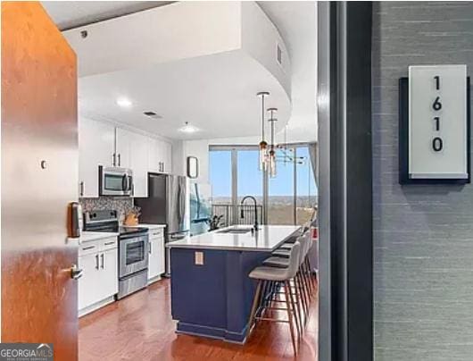 kitchen with white cabinets, appliances with stainless steel finishes, hanging light fixtures, light countertops, and a sink