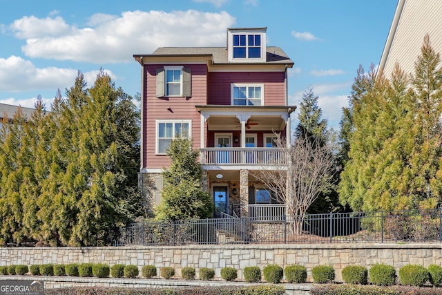 view of front of property featuring a fenced front yard, stone siding, a balcony, and a ceiling fan