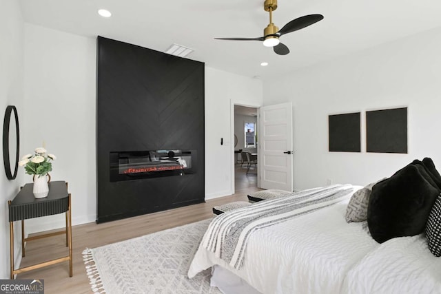 bedroom with a large fireplace, baseboards, light wood-style floors, and recessed lighting